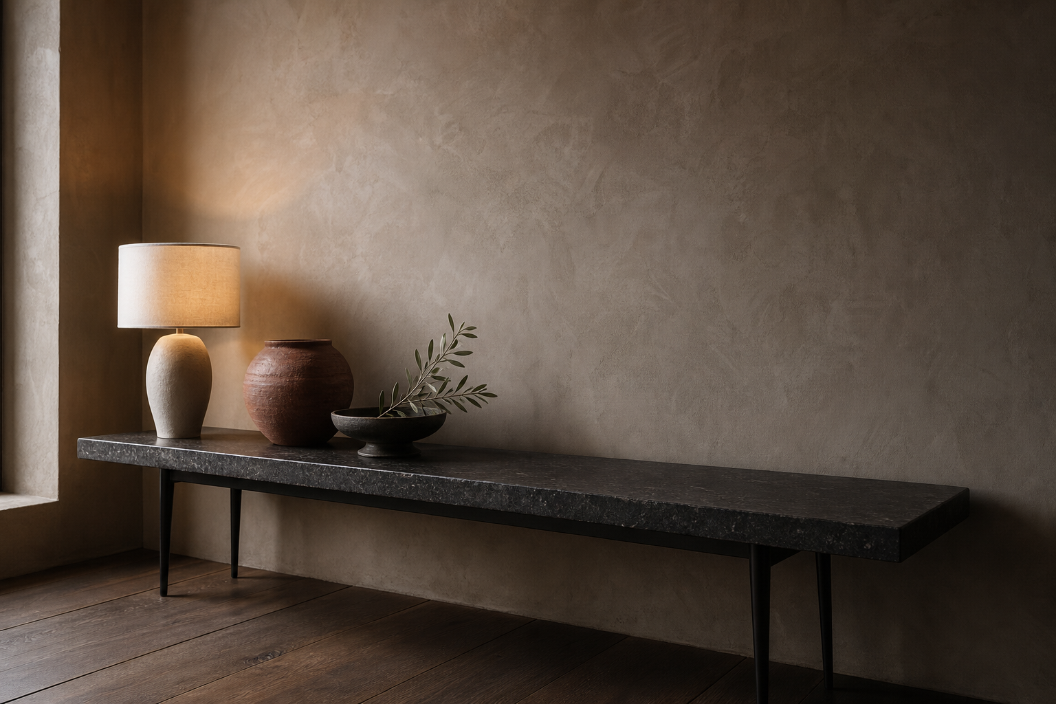 Travertine console table styled with a sculptural ceramic lamp, burnt-clay vessel and single olive branch against a tadelakt wall